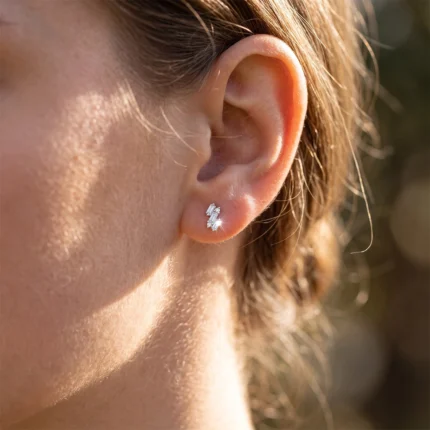 Close-up of an ear with a small silver diamond-stud earring that reflects sunlight.