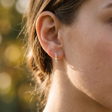 Close-up of a woman's ear with a silver diamond-studded drop earring catching sunlight on the skin surface.