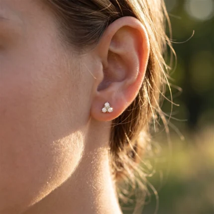Close-up of a pierced earlobe with a small three-diamond triangle stud earring outdoors.