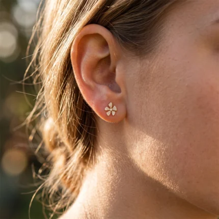 Close-up of a woman's ear wearing a small gold flower-shaped diamond earring on the earlobe