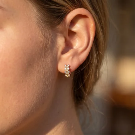 Close-up of an ear wearing a small gold hoop earring set with diamonds along the front of the lobe