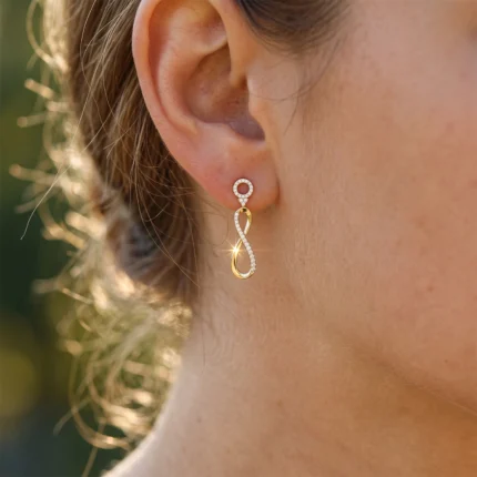 Gold and diamond drop earring with an infinity-loop design worn on the ear.