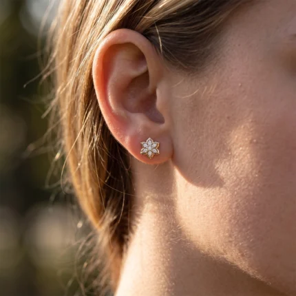 Close-up of a gold flower-shaped diamond earring worn on the earlobe.