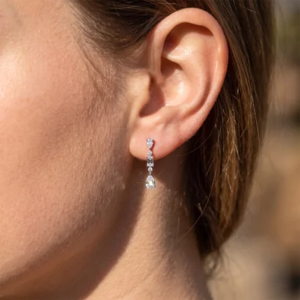 Close-up of a woman's ear wearing a silver drop earring with a teardrop diamond at the bottom.