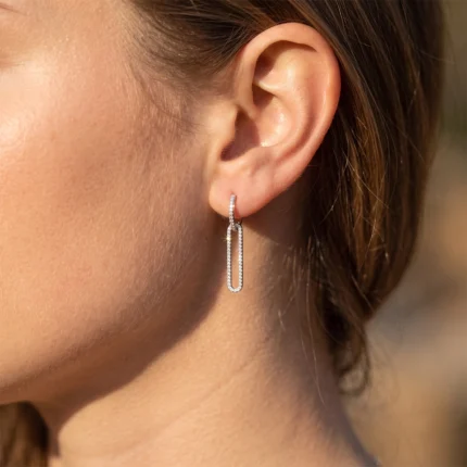 Close-up of a woman's ear wearing a diamond-studded rectangular hoop earring that dangles from the earlobe