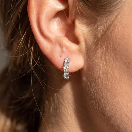 Close-up of a person's ear with a silver hoop earring encrusted with small diamonds on the lobe edge.