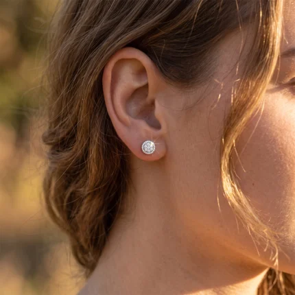 Close-up of a woman's ear with a small round diamond stud earring on the earlobe in sunlight.