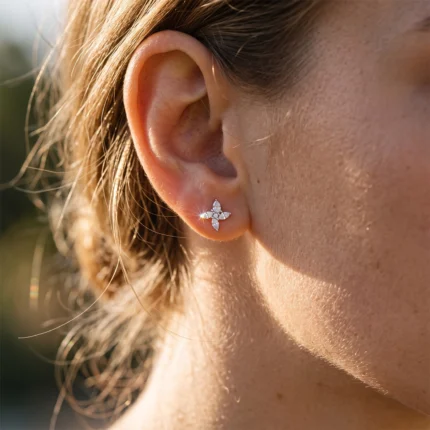 Close-up of a woman's ear wearing a small silver flower-shaped diamond earring, catching the sunlight.