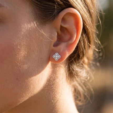 Diamond flower stud earring on the earlobe, featuring four-petal design with small stones surrounding a central gem.