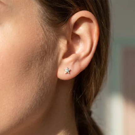 Close-up of a woman's left ear with a small silver star diamond stud in the earlobe.