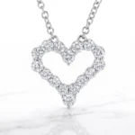 Heart-shaped diamond pendant necklace on a silver chain, with round-cut stones forming the outline against a white background.