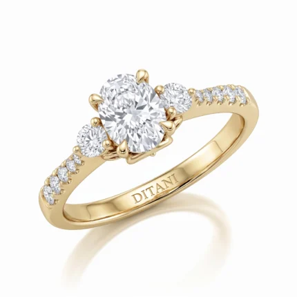 Yellow-gold engagement ring with a large oval center diamond, flanked by two smaller diamonds and pave-set diamonds along the band, seen at an angle.