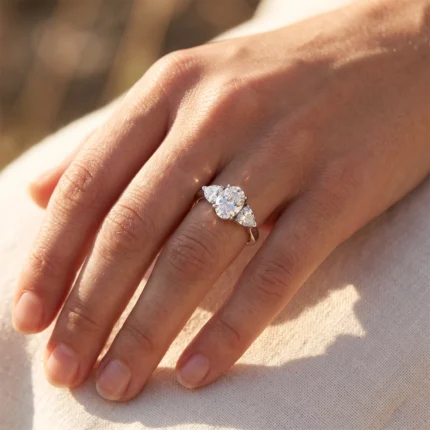 Close-up of a hand wearing an engagement ring: a large central round diamond flanked by two pear-shaped diamonds on a slim band