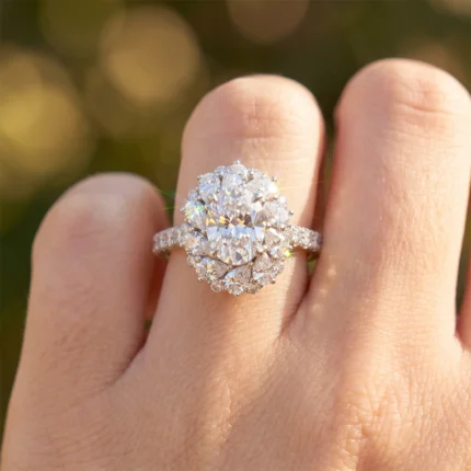 Engagement ring with a large oval center diamond surrounded by a halo of smaller diamonds on a pavé band, worn on the finger.