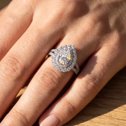 Close-up of a diamond halo ring on a ring finger: large central gem surrounded by double halo of smaller diamonds, set on a silver/white gold band.