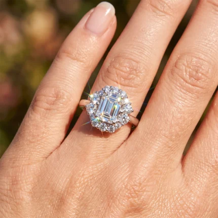 Close-up of a diamond halo ring on a finger, featuring a large emerald-cut center stone surrounded by small diamonds.