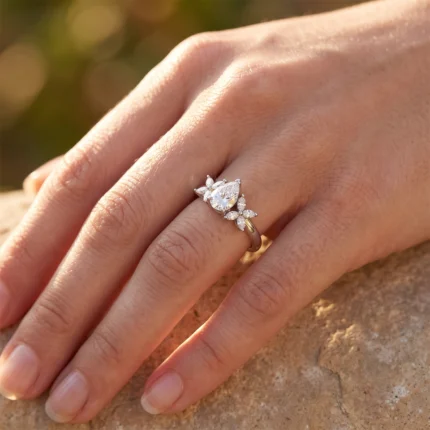 Close-up of a hand wearing an engagement ring: a pear-cut center diamond with surrounding marquise diamonds on a slim two-tone gold band.