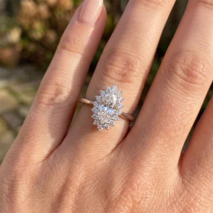 Oval-cut center diamond ring with a halo of small diamonds on a gold band, worn on a finger in sunlight.
