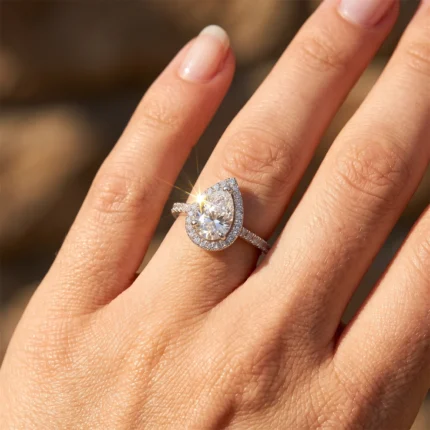 Teardrop (pear-cut) diamond ring with a halo of small diamonds on a finger, sparkling in sunlight.