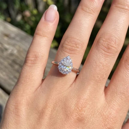 A pear-shaped engagement ring with a halo of small stones on a rose-gold band worn on the ring finger.