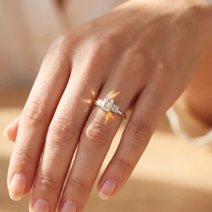 Close-up of a hand wearing a three-stone diamond engagement ring on the ring finger.