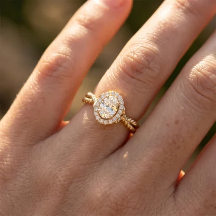 Gold twisted-band engagement ring with an oval center diamond surrounded by a halo of smaller diamonds on a finger.