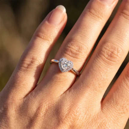 Close-up of a hand wearing a rose-gold ring with a heart-shaped center diamond encircled by tiny diamonds in a halo setting.