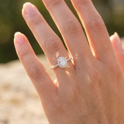 Engagement ring with a halo of small diamonds on a finger, glowing in warm sunlight.
