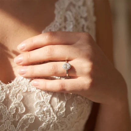 Close-up of a woman's hand wearing a diamond halo engagement ring on the ring finger, resting on lace fabric.