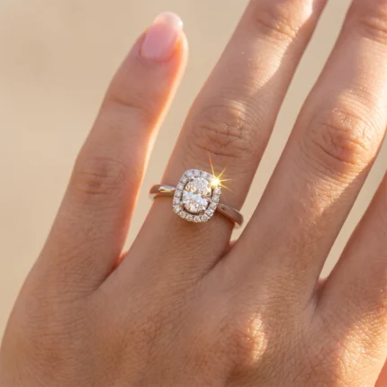 Close-up of a gold engagement ring with a halo of small diamonds and a large center stone on a finger with sunlight sparkle.