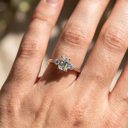Close-up of a rose-gold ring with a rectangular emerald-cut center diamond flanked by two smaller stones on a finger.