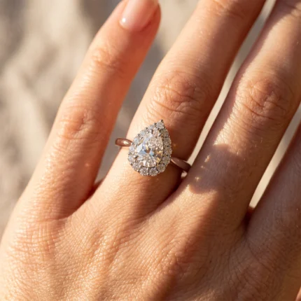 Pear-cut diamond ring with a halo of small diamonds on a finger (rose-gold band)