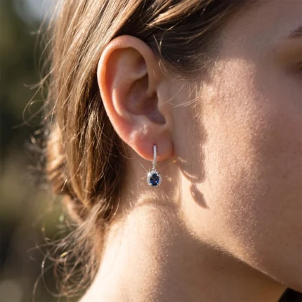 Close-up of a woman's left ear wearing a silver drop earring with a blue gemstone.