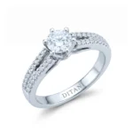 Engagement ring with a central round diamond in a prong setting and pavé diamonds along the band in silver metal.