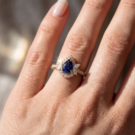 Gold ring with a pear-shaped blue gemstone surrounded by small diamonds on the finger