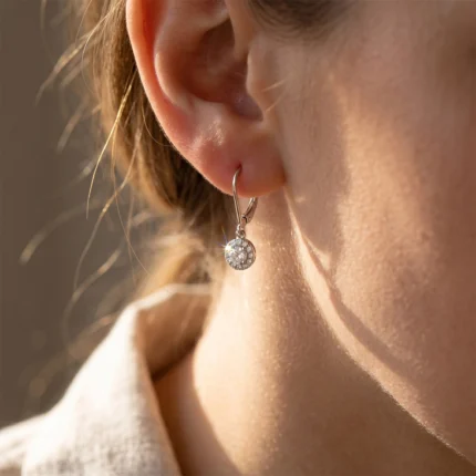 Close-up of a pierced ear wearing a silver hoop with a round, sparkling crystal pendant catching the light